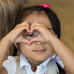 little girl making a heart with her hands over eye