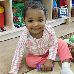 little girl sitting on floor smiling playing with toys in toddler class