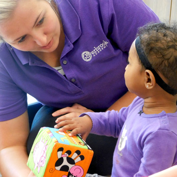 teacher sitting with baby on floor playing with a toy