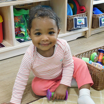 young baby sitting on the floor next to a basket of toys