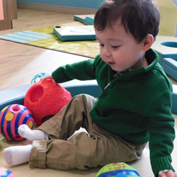 little boy sitting on classroom rug playing with toys